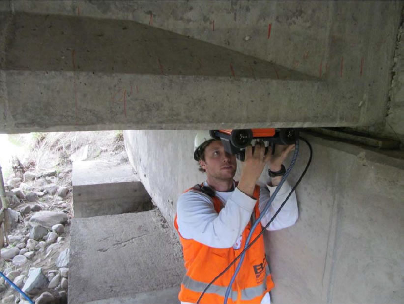 Figure 2 showing GPR scan along bottom of a girdr (typical).  Workman is holding equipment above his head mounted on the girder.
