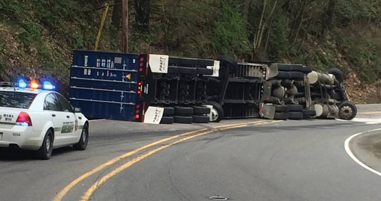 the image is of an overturned semi-truck on NW Cornelius Pass Road.  There is a police car behind the truck with flashing lights on.