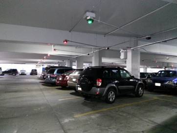 Cars in a parking garage with overhead green and red lights.