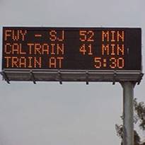 Overhead road signs reading: FWY - SJ 52 min, Caltrain 41 min, train at 5:30.