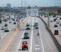 Photo. Overhead signs identifying 'Toll Lane Only' and 'HOV 2+ Only' lanes and vehciles using the lanes in Denver, Colorado.
