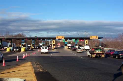 photo of a toll plaza from the point of view of a driver approaching the plaza; both cash lanes and electronic toll collection (ETC) lanes are available among the 10 lanes under one roof stretching across both directions of a highway