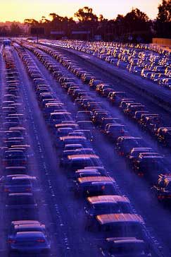 photo of a freeway operating at capacity: four lanes in each direction with long queues of closely spaced vehicles in all lanes