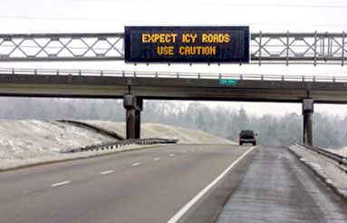 photo of overhead light-emitting matrix message sign mounted over the center of one side of a divided highway with the message "EXPECT ICY ROADS: USE CAUTION"