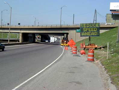 photo of a portable message sign mounted on a trailer next to the outside shoulder of a highway in advance of a work zone. It shows the message "REDUCE SPEED AHEAD"