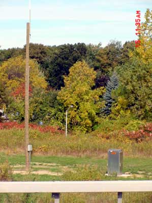 photo of a HAR installation in a field next to a highway, showing a wooden pole with an antenna mounted on top and a ground-mounted cabinet containing the electronic components