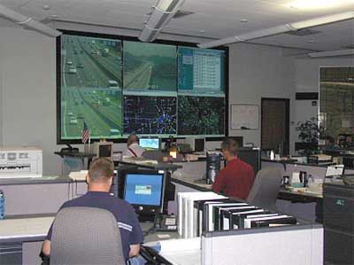 photo of the interior of a TMC, showing operators at workstations and a display wall