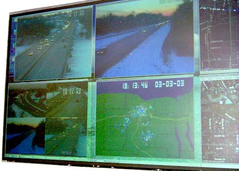 photo of a projection television display wall in a TMC, showing six screens with traffic videos and maps