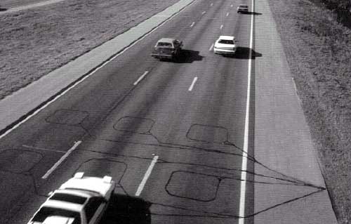 photo of a series of wire loops (a pair of loops in each lane) installed in three lanes of one direction of a highway, with cars driving over the loops