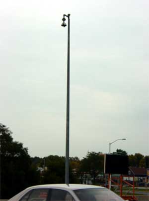 photo of a CCTV camera assembly, showing a camera mounted at the top of a pole located next to a roadway, with a car moving under the camera