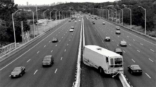photo of a transfer machine changing the position of a moveable barrier on a freeway; the barrier is shown separating four lanes in each direction