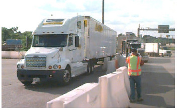 Photo of a data collector standing next to a truck, with a concrete barrier separating them.
