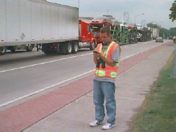Photo of a data collector standing on the roadway shoulder next to a long line of trucks.