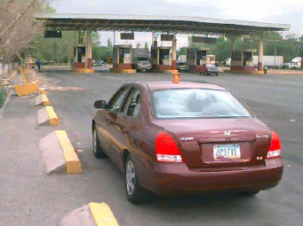 Photo of the primary collection point on the Mexican side of the Zaragoza Bridge, showing cars and trucks exiting the tollbooth. An official's car is in the foreground.