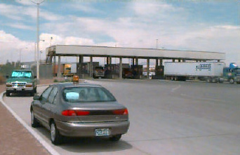 Photo of the primary collection point on the U.S. side of the Zaragoza Bridge, showing trucks exiting the tollbooth. An official's car is in the foreground.