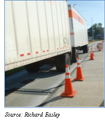 Photograph of a tractor with 2 trailers at a static weigh station. Orange cones line the right side of the truck. Source: Richard Easley.