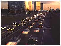 Traffic heads into sunset reflected off tall buildings