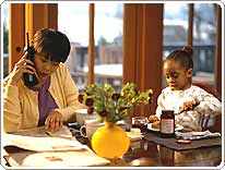 mom talking on phone at kitchen table while daughter spreads jelly on toast