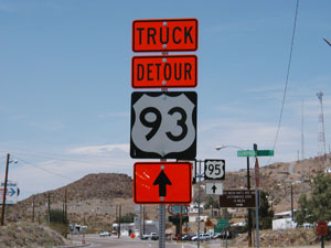 A color picture shows a truck detour route trailblazer sign for U.S. 93. An orange sign that reads “truck detour” is posted above the black and white sign for U.S. 93. An orange sign with an arrow is posted below the sign for U.S. 93.