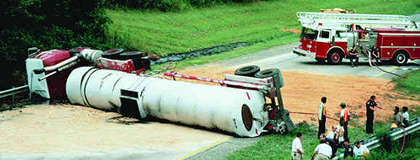 Photograph of overturned tanker truck blocking roadway, with fire truck and crew nearby