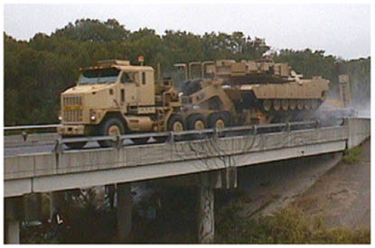 photo of a special-use military transporter, a heavy equipment transport system vehicle, crossing a highway bridge