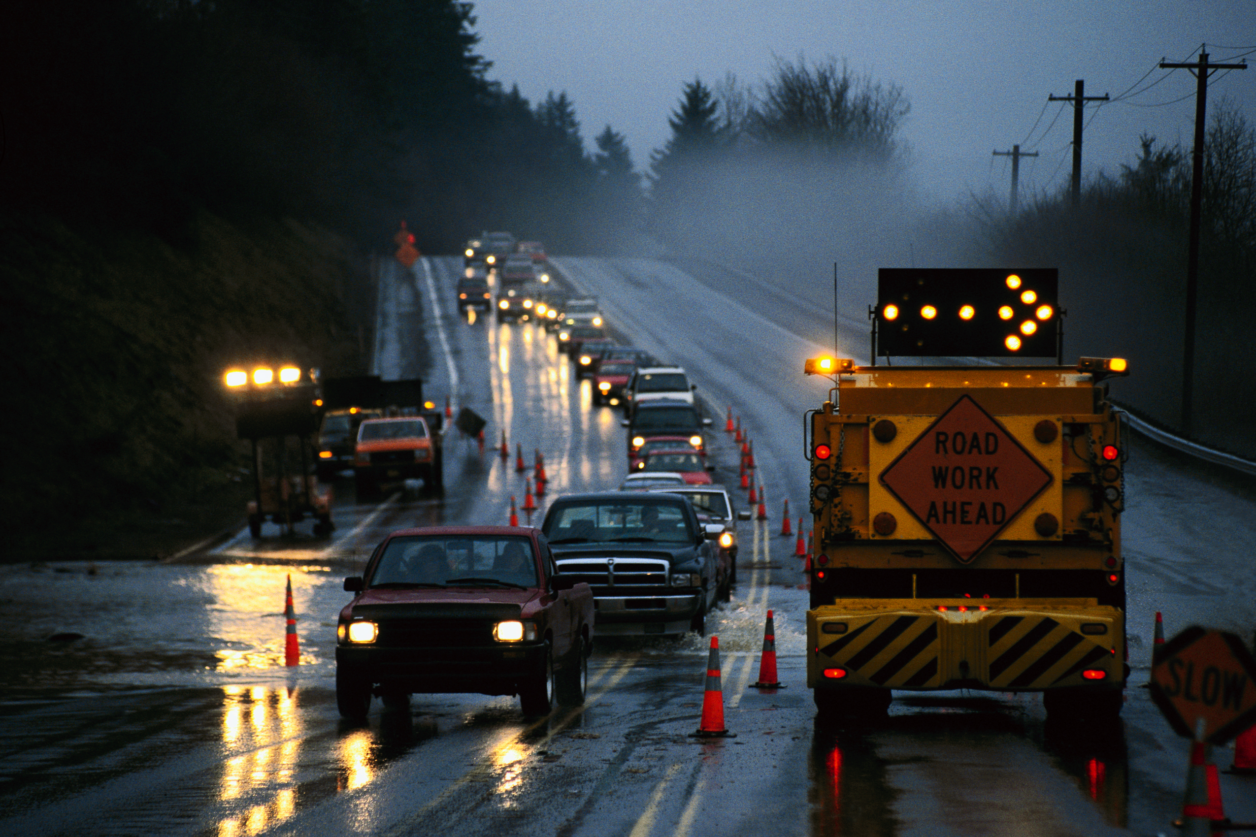 photo of cars on a roadway at night approaching a movable road work ahead sign