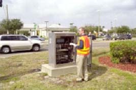 photograph of the project field implementation. It shows an engineer inputting a timing plan into a signal controller and observing traffic flow along the adjacent road.