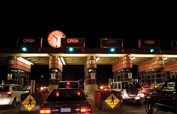 Photo. Cars moving through toll lanes marked Cash on a highway at night.