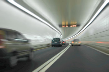 Photo. Cars driving through a tunnel with a digital overhead sign indicating “DELAY AHEAD.”