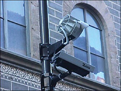 Photo. Close-up view of a typical Automatic License Plate Recognition (ALPR) camera and it’s overhead lighting unit in use on the street.