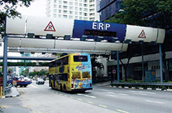 Photo. A large bus driving under a group of transceivers mounted on entry-point gantries as part of the ERP system in Singapore.
