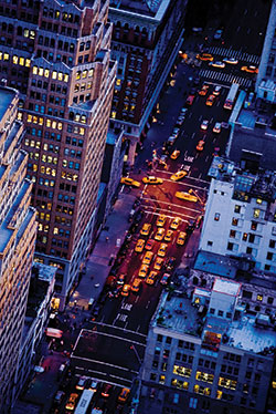 Photo. Overhead view of a large city block, depicting tall buildings and the city traffic on a large street.