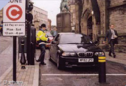 Photo. A manual toll collector on duty taking tolls from a car at a designated street location in Durham City, UK.