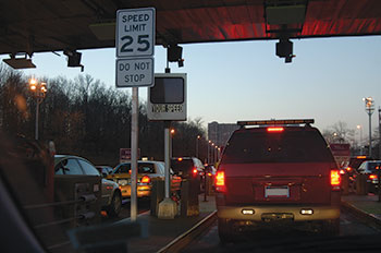 Photo. Traffic moving through a vehicle occupancy detection station, passing a sign reading “Speed limit 25. Do Not Stop.”