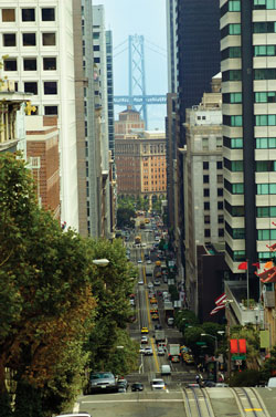 Photo. A view of a typical San Francisco street, with moderate traffic and the Golden Gate Bridge in the distance.