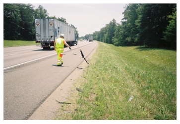 Photo of a man wearing a performance class E safety ensemble removing debris from a highway and placing it on the edge of the shoulder for later pickup.
