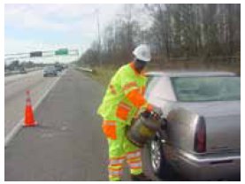 Photo of a service patrol operator adding gas to the tank of a disabled vehicle on the side of a highway.