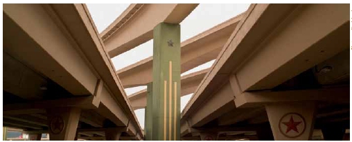 Photograph of the underside of several overpasses. A series of three central pylons shown are painted green and depict three gold verticle lines extending downward from a molded cast of a star.