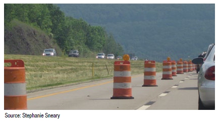 Photo of a two-lane roadway with the left lane showing a taper comprised of construction barrels as the lane is closed. Source: Stephanie Sneary