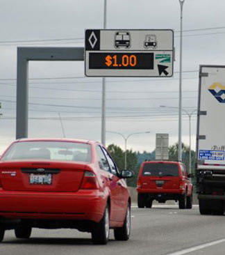 Photo of vehicle on freeway, passing under a sign indicating a $1.00 rate for use of the HOT lane.