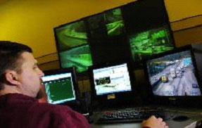 Photo of a man sitting at a computer terminal with several screens monitoring traffic flow.