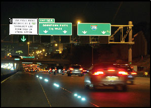 Photo of nighttime traffic on the I-35 W MnPASS facility, showing a sign gantry with a sign indicating that the dynamic shoulder lane is open.