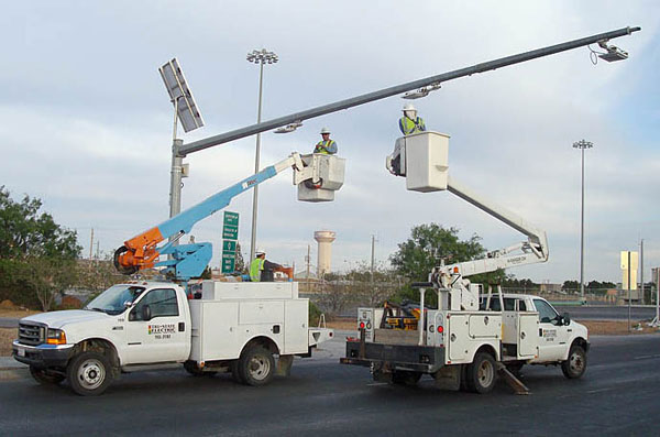 Figure 10. Photo. Installing RFID antennae on a mast arm. Two trucks with cherry pickers are parked under a traffic-signal-type pole with a cantilever arm. The men in the cherry pickers are installing equipment on the cantilever arm.