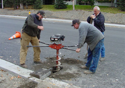 Photo of three men using an auger to drill a hole into the shoulder of a road to install an MRC temperature probe. 