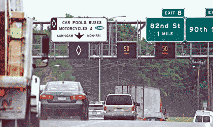 Picture of vehicles on a highway with the far left lane designated as a High-Occupancy Vehicle lane for car pools, buses, motorcycles, and MnPASS users 6 a.m. to 10 a.m Monday to Friday with a High-Occupancy Vehicle diamond symbol on an electric sign directly above the lane, and the other two lanes labeled with electronic “50 miles per hour” signs above each lane.