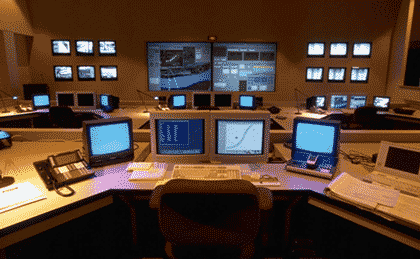 Picture of a transportation management center control room with a computer console in the foreground and a video wall in the background.