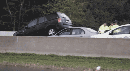 Picture of a crash along a median barrier with one vehicle sitting on top of the hood of another.