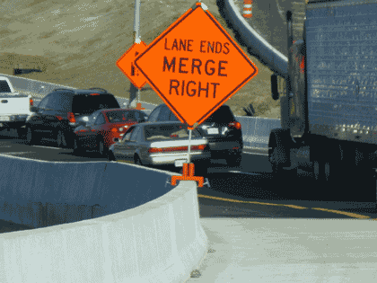 Picture of a workzone along a highway with a “Lane Ends Merge Right” sign on a median barrier.