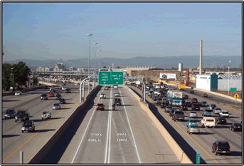 A photograph of two lanes of interstate marked as toll separated by barrier from general lanes of congested traffic.