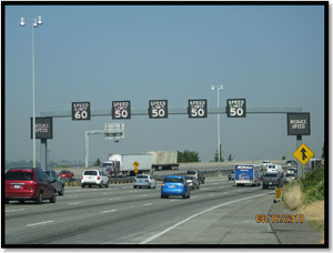 Photo - Picture of interstate travels, cars traveling under a sign structure of variable speed limts.